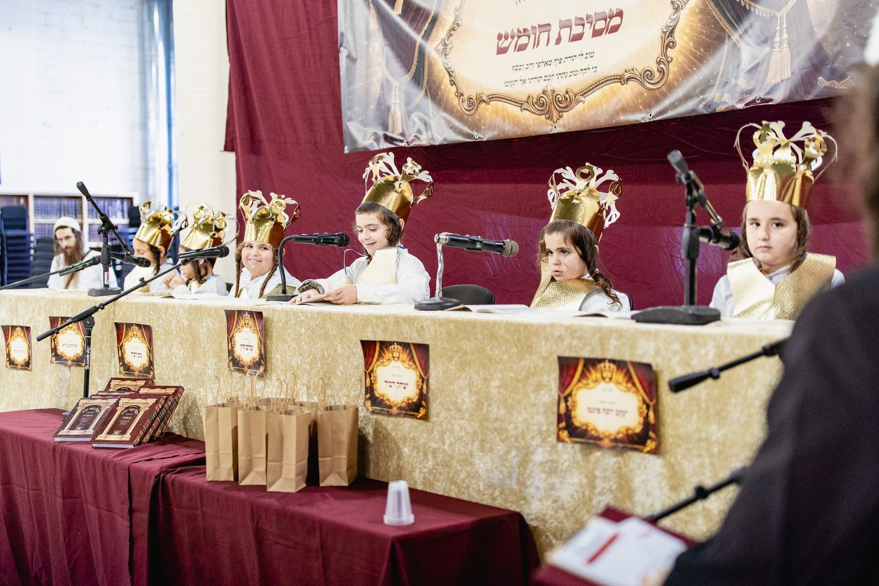 Boys in gold crowns at the Mesibat Chumash head table, with Chumashim and gifts in front